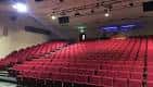Interior del auditorio con filas de butacas rojas y escenario iluminado