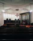 Interior del salón de culto con banco de órgano y cruz en la pared