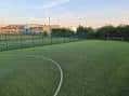 Campo de fútbol exterior con césped artificial y valla perimetral al atardecer