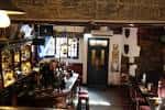 Interior acogedor del pub con barra de madera, estanterías decoradas y mesas
