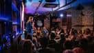 Interior del club de comedia con público y artista en el escenario bajo luces de colores