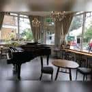 Interior del café con piano de cola y mesas junto a ventanales