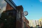 Fachada exterior del edificio del local Commune con reloj colgante bajo cielo azul