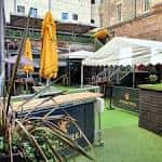 Área al aire libre de Bar 50 con sombrillas amarillas y zona verde