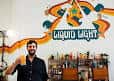 Persona sosteniendo una cerveza en el interior del taproom de Liquid Light Brewing Company