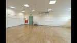 Sala interior espaciosa con suelo de madera clara, paredes blancas y iluminación artificial