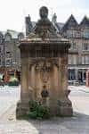 Frente principal del West Bow Well con escudo heráldico y entorno urbano de Grassmarket
