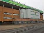 Fachada exterior del estadio Carrow Road con letrero 'Woodford Lane'
