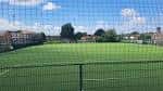 Vista del campo de fútbol artificial con valla perimetral y cielo despejado