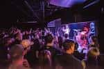 Vista interior del club con una banda tocando en el escenario y público animado