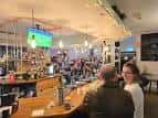 Ambiente interior del pub con clientes sentados en el bar y pantalla de televisión