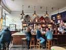 Interior del pub con clientes sentados en el mostrador y decoración tradicional