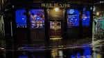 Fachada nocturna del pub The Blue Blazer iluminado con reflejos en la calle mojada