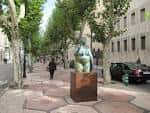 Vista del paseo con árboles alineados y escultura central durante el día