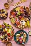 Vista cenital de tablas de aperitivos con frutas y quesos sobre fondo rosa