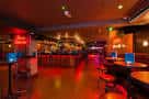 Interior del bar con barra iluminada y mesas para clientes