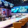 Interior del bar Cry Baby con barra larga y pantallas de neón