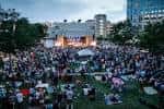 Concierto al aire libre en Gallivan Center con escenario iluminado y multitud sentada en la hierba