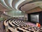 Interior del auditorio con butacas en gradas y pantalla de proyección