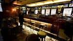 Área interior del pub con barra larga y taburetes bajo iluminación cálida