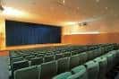 Sala de conferencias o auditorio secundario con butacas verdes y telón azul