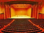 Interior del auditorio principal con butacas rojas y escenario iluminado