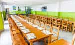 Interior del comedor escolar con largas mesas de madera y sillas, apto para banquetes o reuniones