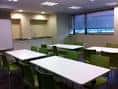 Sala de reuniones o aula interior con mesas blancas y sillas verdes