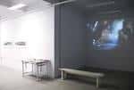 Interior del espacio de exposición con proyección audiovisual y banco