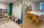 Aula de actividades con mesa y sillas infantiles, y zona de juego decorada con guirnaldas.