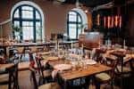 Interior del salón de eventos con mesas de madera rústicas y grandes ventanas arqueadas