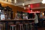 Interior del bar con barra de madera, taburetes y luces colgantes