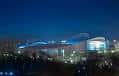 Exterior del estadio Falmer iluminado de noche, bajo un cielo azul oscuro