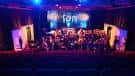 Escenario iluminado con luces de colores y una orquesta o grupo actuando