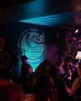 Ambiente nocturno en The Folklore Rooms con el logo iluminado en azul y público