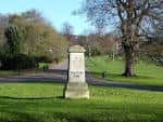 Mojón de piedra con inscripción en una zona de césped y árboles de Preston Park