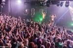 Interior de un local de música en directo lleno de gente, con iluminación de escenario