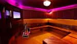 Interior de una sala privada de karaoke con iluminación ambiental magenta y asientos de esquina