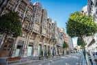 Calle con edificios históricos de fachadas ornamentadas y árboles en el centro de Oviedo