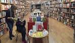 Interior de la librería con perspectiva del pasillo central y clientes consultando libros.