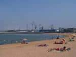 Vista a nivel de la arena de la Playa de El Arbeyal con bañistas y estructuras portuarias al fondo