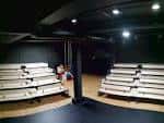 Interior del espacio escénico con gradas de madera modulares y configuración de teatro de caja negra