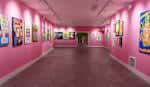 Pasillo de exposición de la Helm Gallery con paredes de color rosa vibrante y obras de arte.