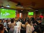 Ambiente interior del pub con asistentes disfrutando de un evento proyectado en pantalla grande