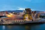 Vista exterior nocturna del Museo Guggenheim Bilbao iluminado junto a la ría