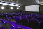 Interior de una sala de cine con butacas moradas y pantalla grande