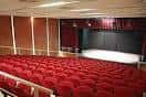 Interior del auditorio con butacas rojas y escenario iluminado