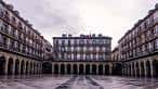 Vista simétrica de la Plaza de la Constitución vacía, destacando las arcadas y balcones bajo un cielo nublado