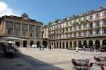 Vista panorámica de la Plaza de la Constitución en un día soleado, mostrando el edificio principal y terrazas de café