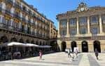 Perspectiva de la Plaza de la Constitución con el antiguo ayuntamiento y gente paseando en un día soleado